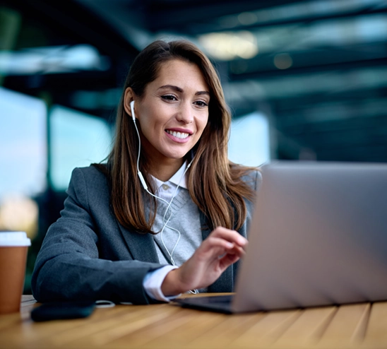 woman with earbuds in smiling and working on her laptop